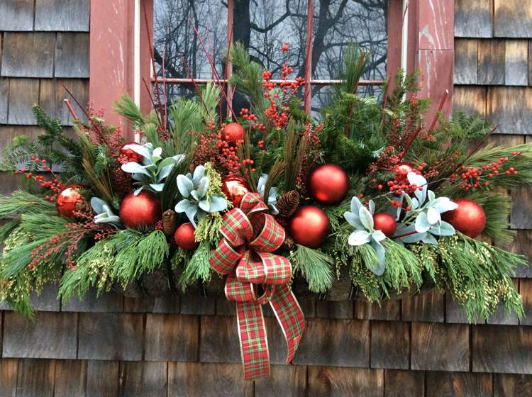 Juldekorationsidéer för fönsterbrädan utanför ordnar röda julbollar och röd diamantbåge och grangrön och bär och cypressgrenar i blomlådan