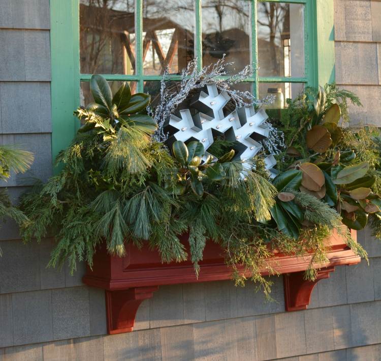 Juldekoration utanför fönsterbrädan Ordna grangrenar och höstlöv och upplysta snöflingor av metall i blomlådan