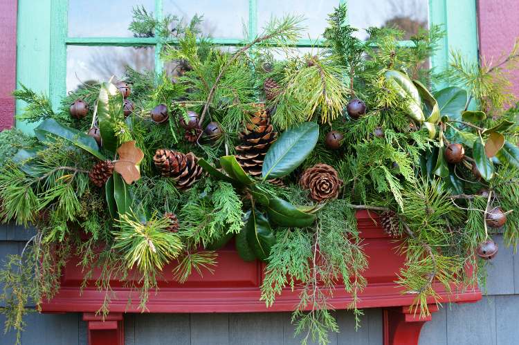 Juldekoration utanför fönsterbrädan Ordna tallkottar och färska blad och tallgröna och julklockor i blomlådan