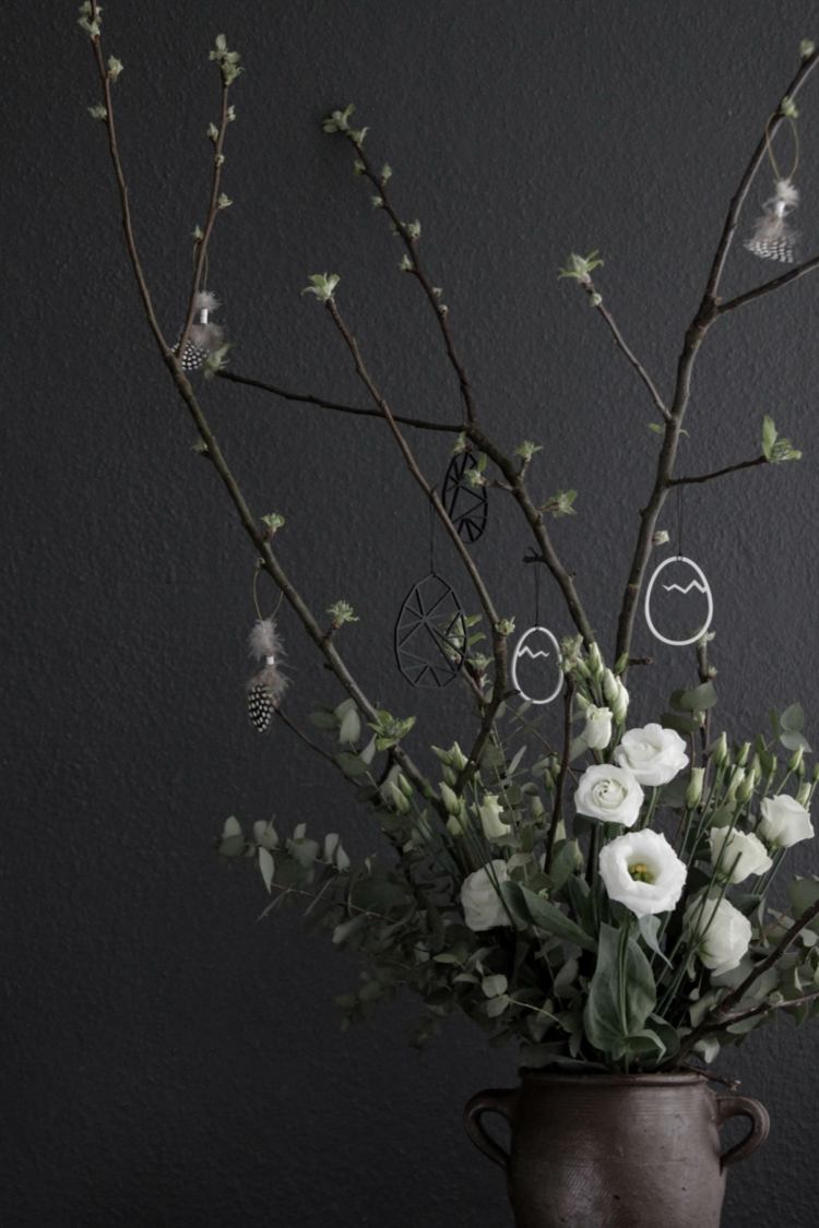 Påskbuske med en kombination av kvistar och vita blommor och fjädrar som dekoration