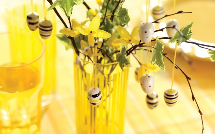 Gul påskbuske med små påskägg av trä och gula blommor