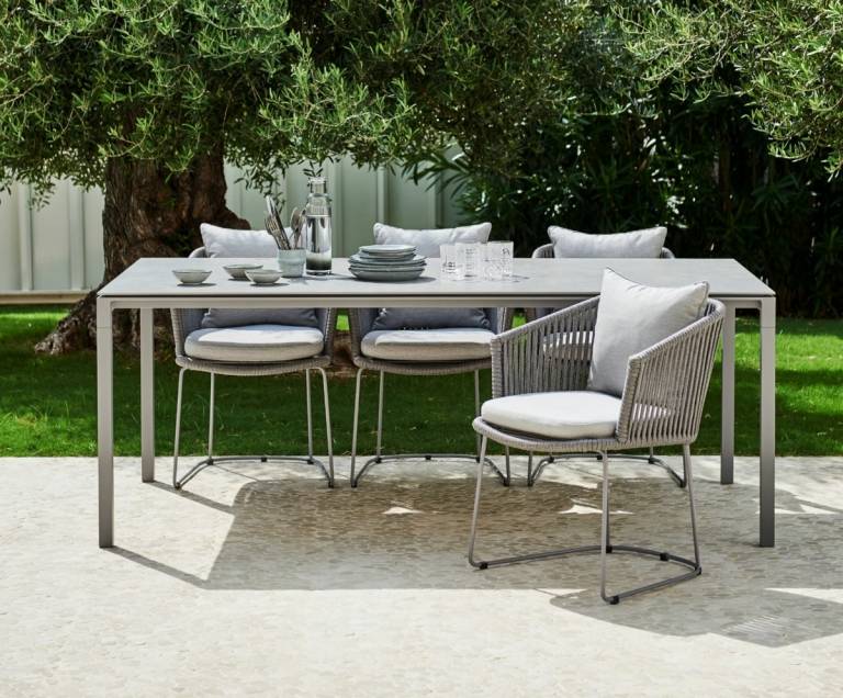 Snyggt matbord med matchande stolar i en vävd design för familjemiddagar i trädgården