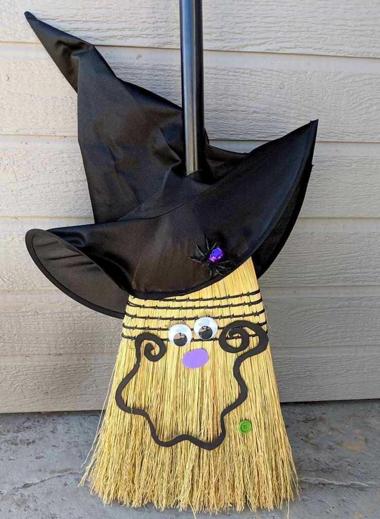 Rolig dekoration för Halloween med ett ansikte på en kvast och häxmössa