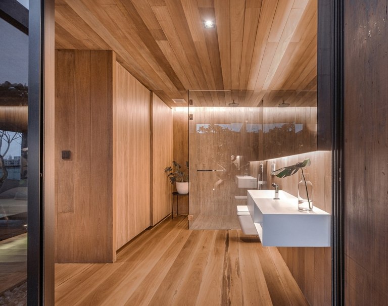 Badrum i trä med en skiljevägg framför duschen och ett vitt handfat