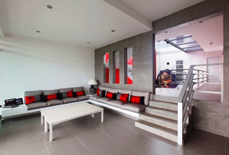 Vardagsrum i grå hörnsoffa-öppen-planering-accenter-röda kuddar-soffbord-vita-trappor