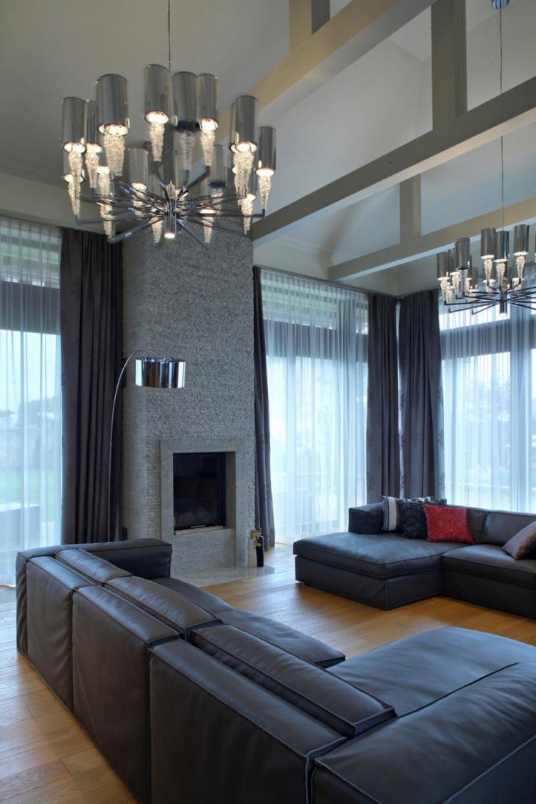 vardagsrum-grå-hörn-soffa-öppen spis-väggbeklädnad-natursten-läder-soffa-ljuskrona-högt i tak