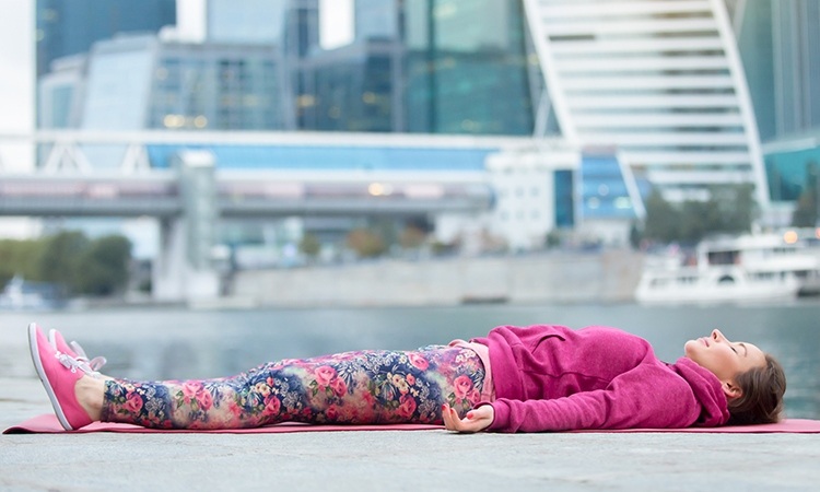 yoga-nidra-till-sömn-praktiska-sömn-övningar-bättre-sömn-djup avslappning-kvinna-liggande-utanför-sov-flod-byggnad